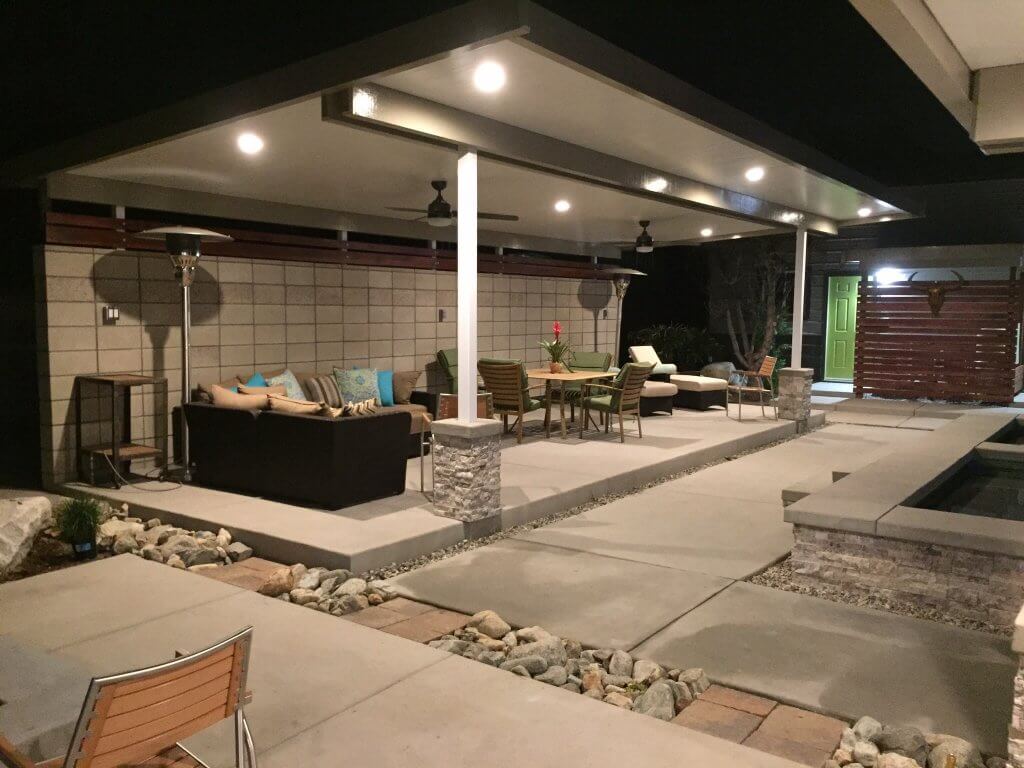 A nighttime patio featuring a pool and stylish furniture, illuminated by soft lighting.